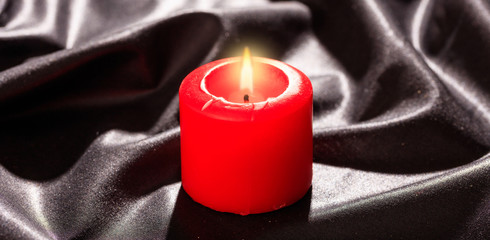 Red candle on black satin background