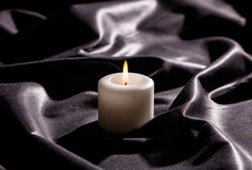 White candle on black satin background