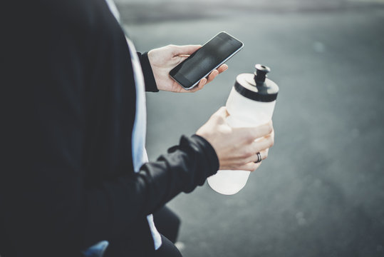 Closeup image of female jogger using modern smartphone outside, young hipster fintess woman checking her results via an app on cellphone after intensive workout, healthy and sport lifestyle