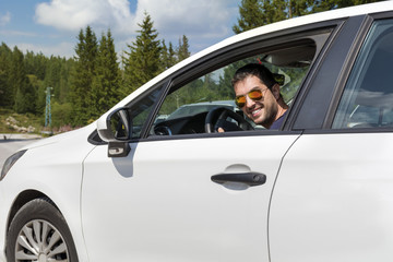 Handsome young man smiling and driving his new white car