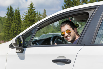 Handsome young man smiling and driving his new white car
