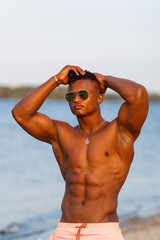 Muscular young athletic sexy man on the beach with a naked torso in underwear. Hot black beautiful guy, fitness model with a rangy sports body.