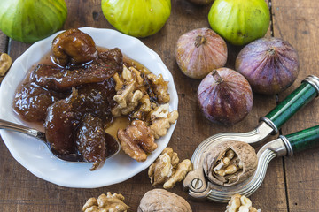Obraz na płótnie Canvas Fig jam with nuts in white dish and several fig fruits and nuts on wooden background