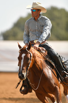 The front view of a rider in cowboy chaps, boots and hat on a horseback running ahead