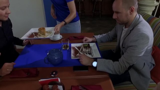 Waitress is putting desserts on a table