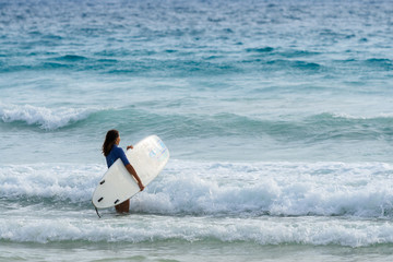 Girl with surfboard going to the sea at surf spot.
