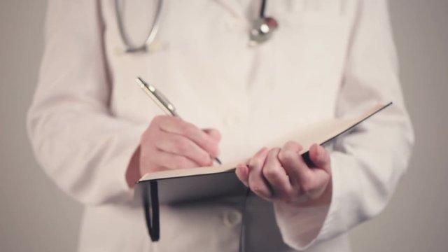 Female doctor in white uniform writing notes after medical exam in her notebook