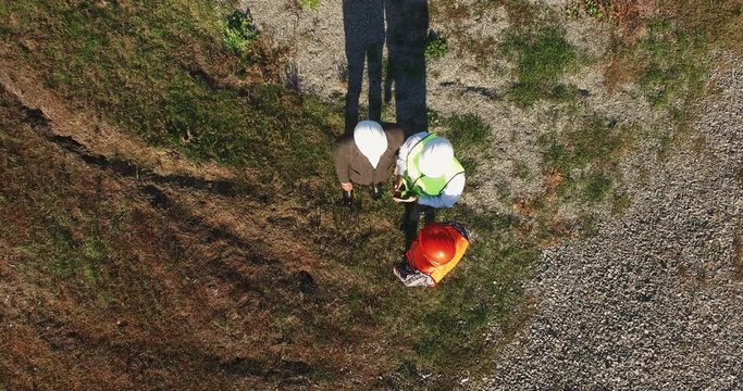 Three technicians, builders, workmen or architects wearing hardhats having a meeting outdoors, on site in a field, overhead view