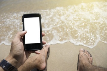 Closeup on a man hand holding smart phone on the beach.laying at the beach.outside background.sunny day.selective focus.light effect added.blurred blue sea and sky in background