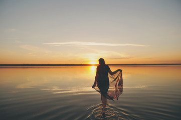 Женщина идет по воде на закате солнца