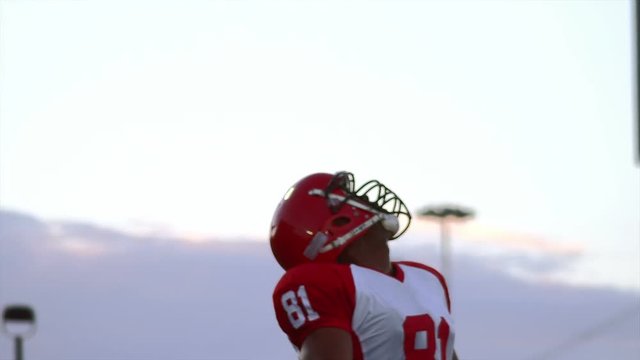 A football player runs towards the camera and catches a pass over his shoulder