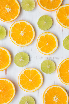 Orange slices and green lemon on white rustic wooden background, top view, flat lay, summer and healthy concept