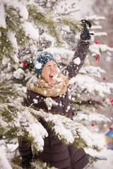 Portrait of happy smiling young woman having fun and playing with snow under Christmas tree. Girl walking in the winter park. Christmas and winter concept.