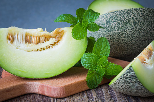 Fresh green melons sliced on rustic wooden table over wall background