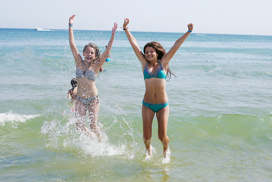Happy girl jumping in the sea raising his hands up
