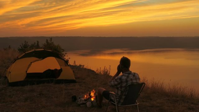 
4K. Harmony of traveler .Waiting sunrise near lake near bonfire.  
