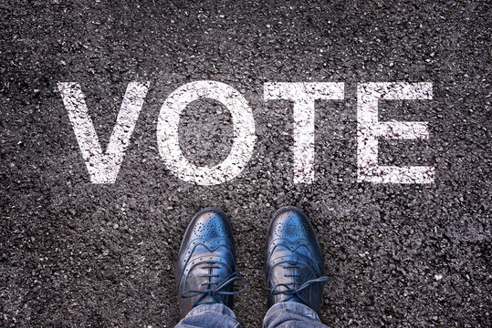 Legs and shoes on asphalt with the word "vote"