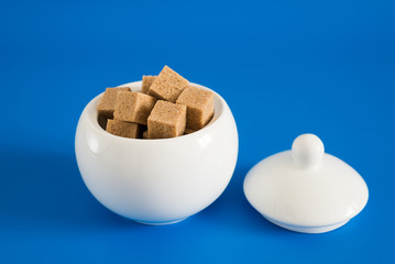 Slices of raw sugar in sugar bowl on blue background