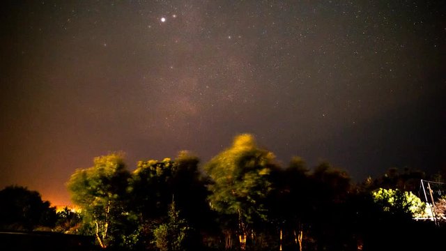 A timelaspe shot of the milky way at night above trees with clouds passing through to give it depth