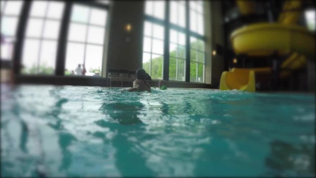 A boy sliding down the water slide at swimming pool to his mother