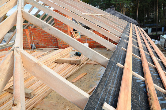 wooden roof construction. house building. Installation of wooden beams at construction the roof truss system of the house. Installing the vapor barrier on the roof
