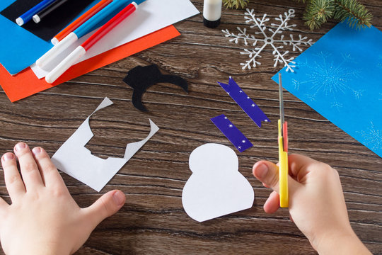 The child cut paper details snowman. The child makes a greeting