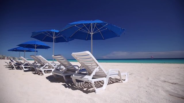 Caribbean beach with blue sun umbrellas and white plastic beds