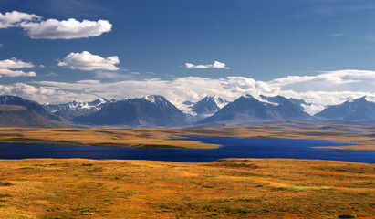 Clean deep blue lake on the background of snow ice covered mountains and glaciers rocks white clouds and bright sky, Plateau Ukok, Altai, Siberia, Russia