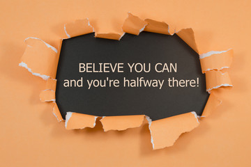 The text Believe you can and you're halfway there, appearing behind torn brown paper. Motivational quote.