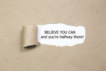 The text Believe you can and you're halfway there, appearing behind torn brown paper. Motivational quote.