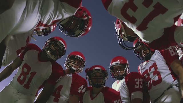 The camera looks up into a huddle full of football players talking before a play