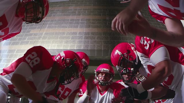 A team of football players huddle and clap to get hyped and ready for the game