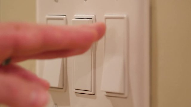 A hand turns on light switches in dark room