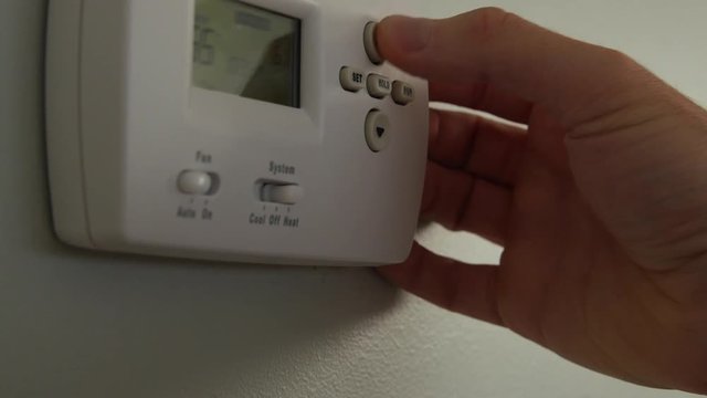 A dolly shot of a man turning up the temperature on thermostat