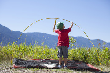 Little boy, age 6 setting up a tent during summertime on the shoreline of Lake Pend Oreille, Sandpoint, Idaho.