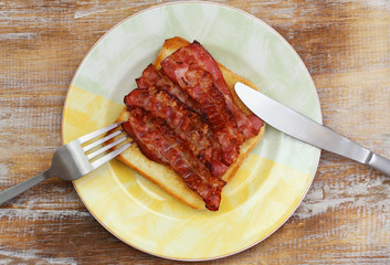 Crispy bacon on white toast on rustic wooden surface, closeup
