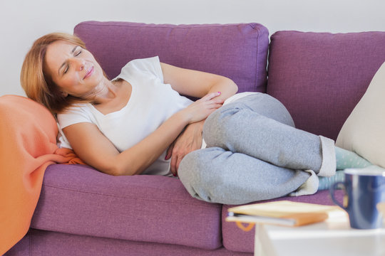 Woman frowning having stomachache sitting on the couch 
