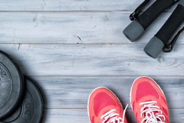 Fitness concept, pink sneakers, dumbbells and weight plates on wooden background, top view
