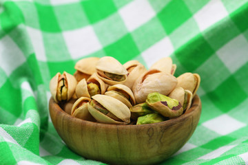 Pistachio nuts in wooden bowl on checkered cloth with copy space
