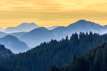 Sunset in bavarian mountains. Blue peaks, green forest and colorful sky. Alps, Germany