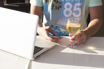 Cropped image of man with telephone, laptop and glass of white wine outdoor