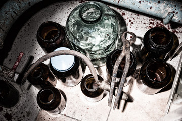 Top view of glass jars, sickle and tongs with blood spattered wa