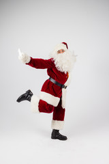 Santa Claus in eyeglasses and red costume dancing and looking into camera on white background. Medium long shot