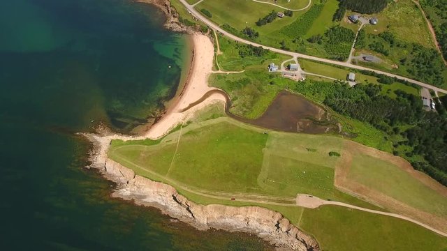 Aerial high shot of farmer cutting grass on a field by ocean cove