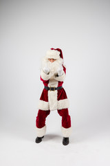 Santa Claus in eyeglasses and red costume standing on white background make a point with hands and looking into camera. Medium long shot
