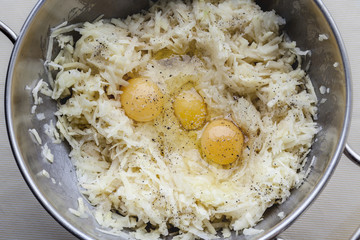Grated potato and three eggs with seasoning for latkes in metal bowl from above