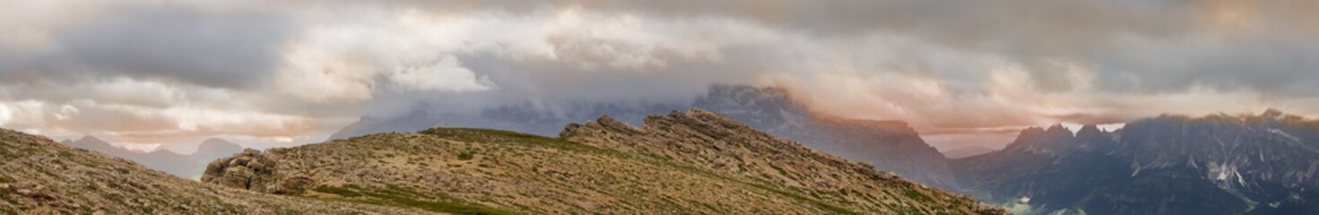 Panoramic mountain peak view from the Settsass in the Dolomites with warm colored cloudscapes hanging on the surrounding rocks.