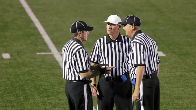 Three football referees stand in a group and discuss a offsides penalty