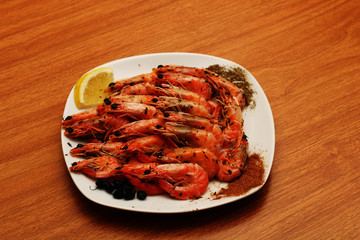 Tasty cooked shrimp lying on a plate with lemon and a variety of spices.