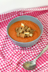 Gazpacho in a bowl with bread pieces on red checkered napkin. Selective focus.
